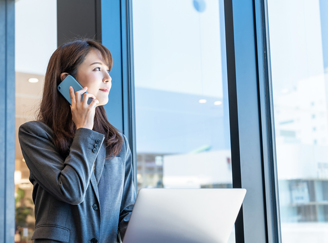 woman using cell phone and looking out a large office window
