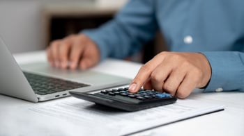 Business professional using a calculator beside a laptop and financial documents