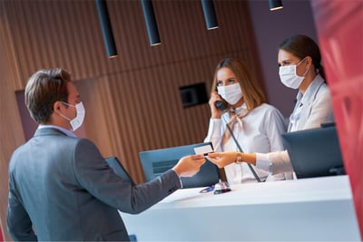 hotel guests talking to receptionists wearing masks
