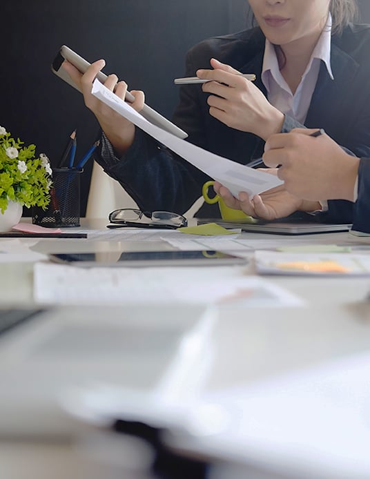 Accounting professional discussing succession planning with coworker at a table covered in paperwork